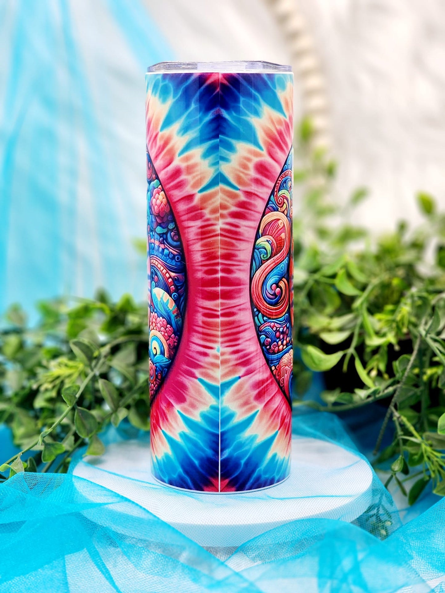 A multicolored tumbler with a peace sign design, placed on a blue background with green leaves around it.
